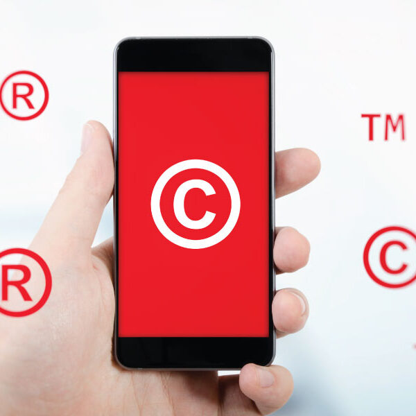 Mano sosteniendo un celular con símbolos de copyright y marcas registradas, representando el registro de marca ante el IMPI.