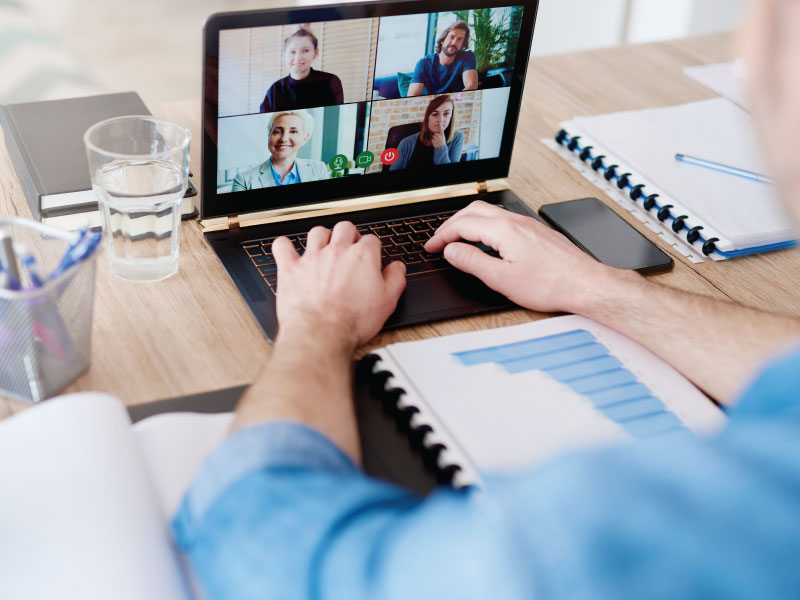 Hombre frente a computadora en casa con videollamada de equipo.